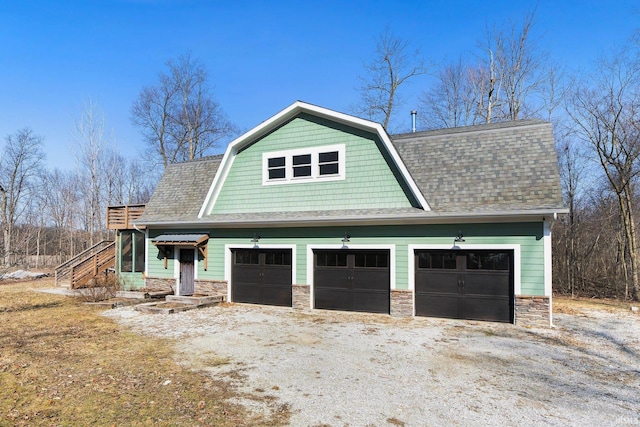 view of front of property featuring stone siding, a garage, a gambrel roof, and roof with shingles