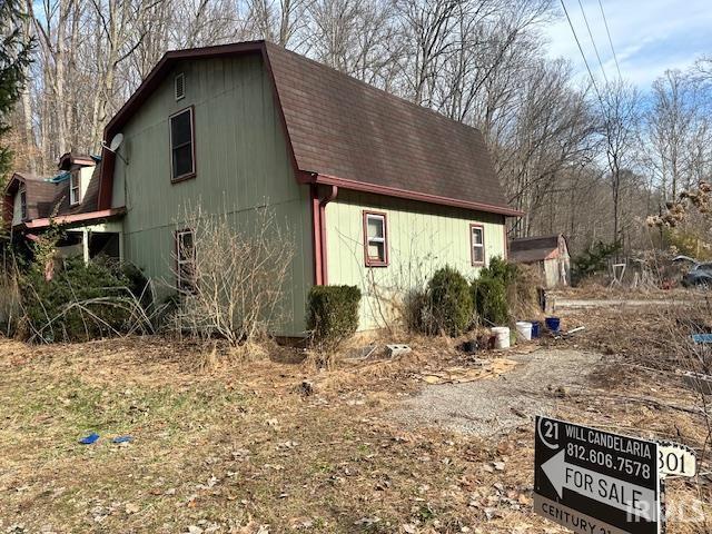 view of side of home with a gambrel roof and roof with shingles