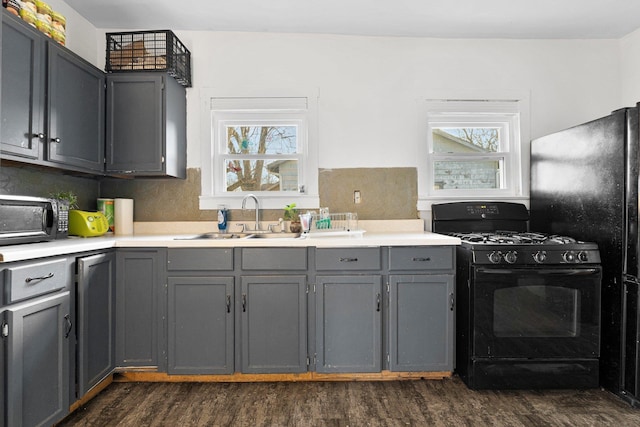 kitchen with dark wood finished floors, light countertops, gray cabinets, black appliances, and a sink