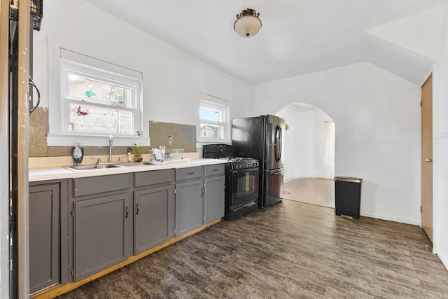 kitchen with dark wood-type flooring, black appliances, gray cabinets, a sink, and arched walkways