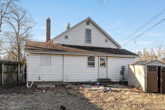 back of property featuring fence, a shingled roof, entry steps, an outdoor structure, and a storage unit