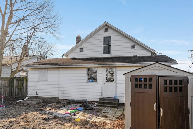 rear view of property with fence, a shed, entry steps, roof with shingles, and an outdoor structure