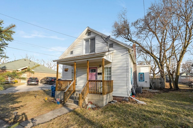 view of front of property featuring a front lawn, cooling unit, covered porch, and a chimney