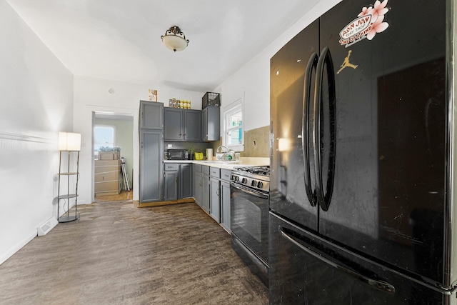 kitchen with black appliances, gray cabinetry, a sink, dark wood-style floors, and light countertops