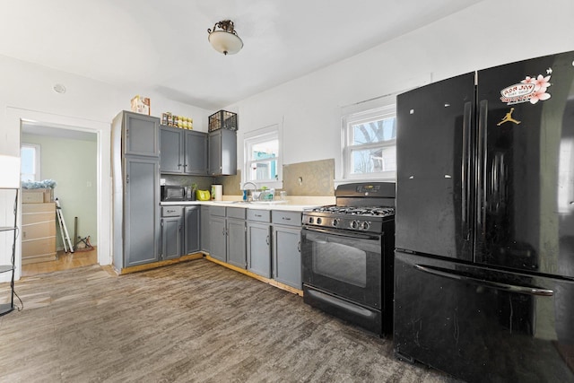 kitchen featuring black appliances, gray cabinetry, a sink, wood finished floors, and light countertops