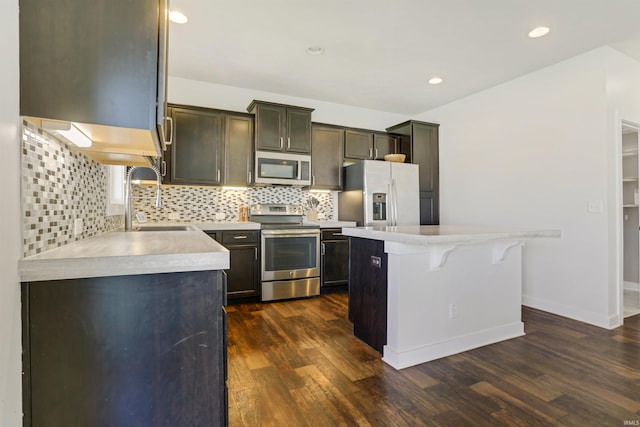 kitchen with a sink, a kitchen island, light countertops, stainless steel appliances, and dark wood-style flooring