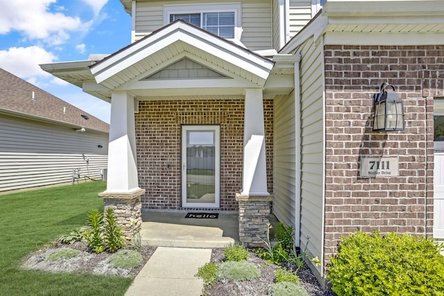 view of exterior entry with a yard and brick siding