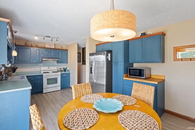 kitchen featuring under cabinet range hood, light countertops, appliances with stainless steel finishes, blue cabinets, and a sink