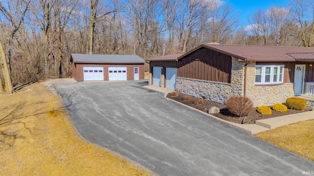 view of front facade with board and batten siding, metal roof, a garage, an outbuilding, and stone siding