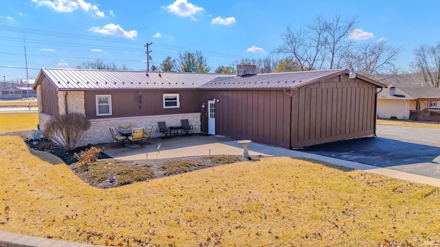 rear view of house with metal roof, stone siding, a yard, and a patio