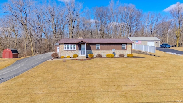 ranch-style home with a front yard, an outbuilding, driveway, stone siding, and metal roof