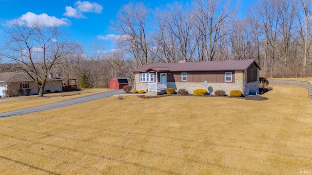 ranch-style house with stone siding, driveway, metal roof, and a front yard