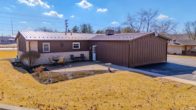 rear view of property featuring a chimney, metal roof, a yard, a patio area, and stone siding