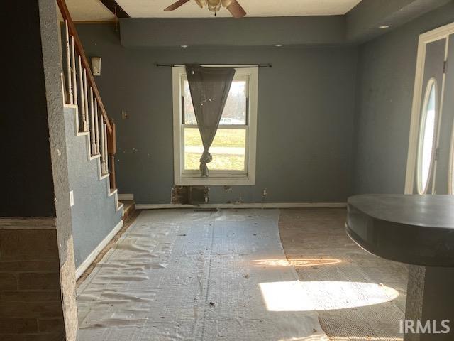 unfurnished living room featuring stairway, baseboards, and ceiling fan