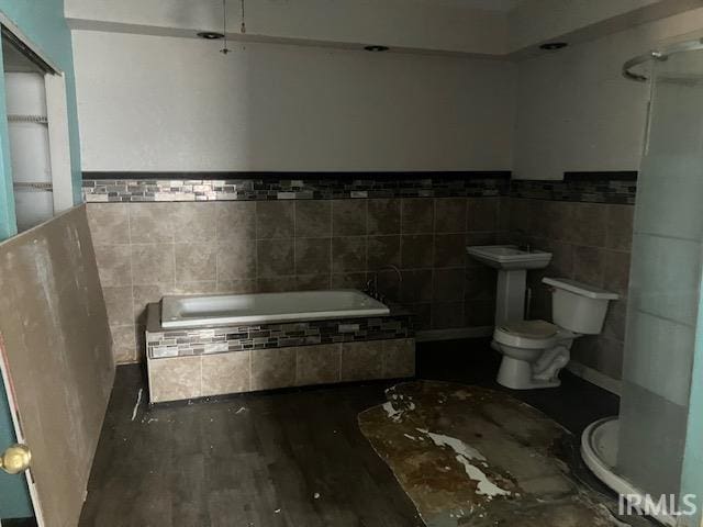 full bathroom with a relaxing tiled tub, toilet, tile walls, and wood finished floors