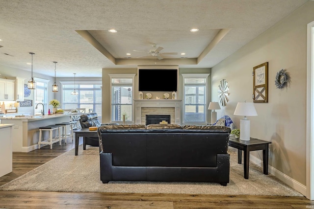 living area with baseboards, a fireplace, dark wood-type flooring, a textured ceiling, and a raised ceiling