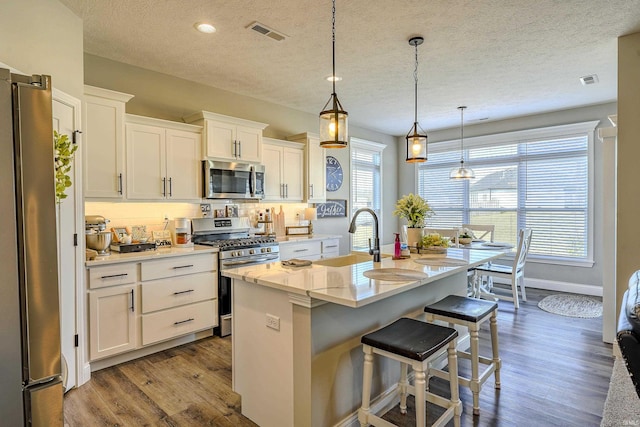 kitchen featuring visible vents, a sink, appliances with stainless steel finishes, white cabinets, and dark wood-style flooring