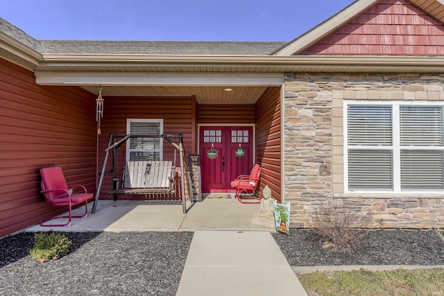 property entrance with a porch, stone siding, and a shingled roof