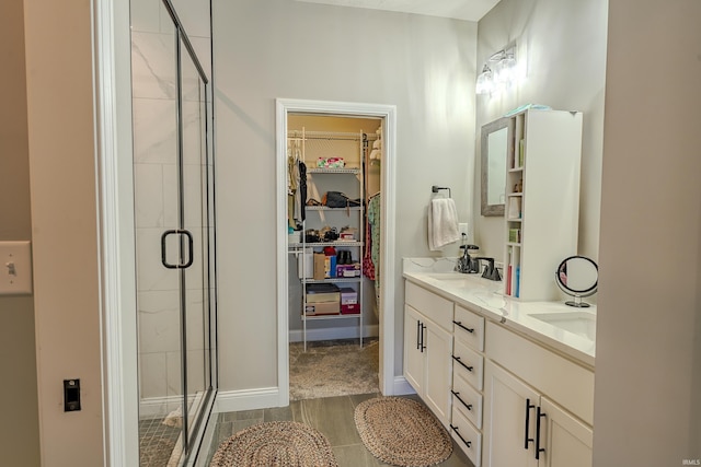 full bathroom with double vanity, a walk in closet, baseboards, and a shower stall