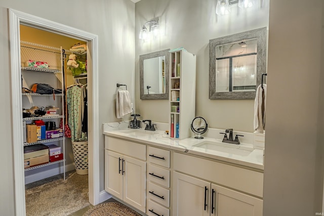 bathroom featuring a sink, baseboards, double vanity, and a spacious closet