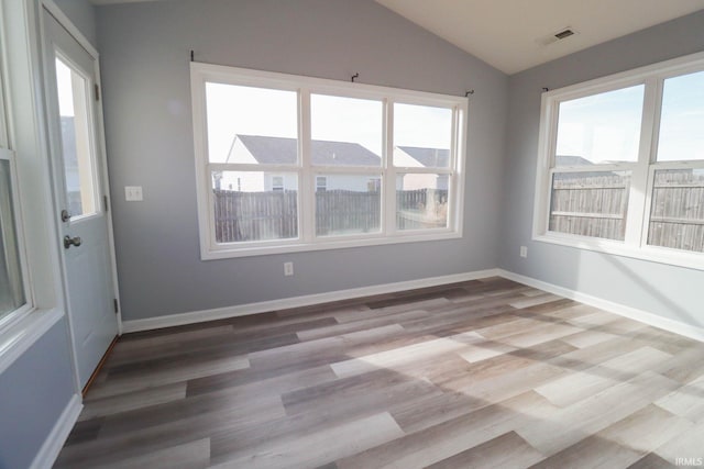 spare room with vaulted ceiling, wood finished floors, baseboards, and visible vents