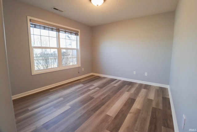 spare room with visible vents, baseboards, and dark wood finished floors