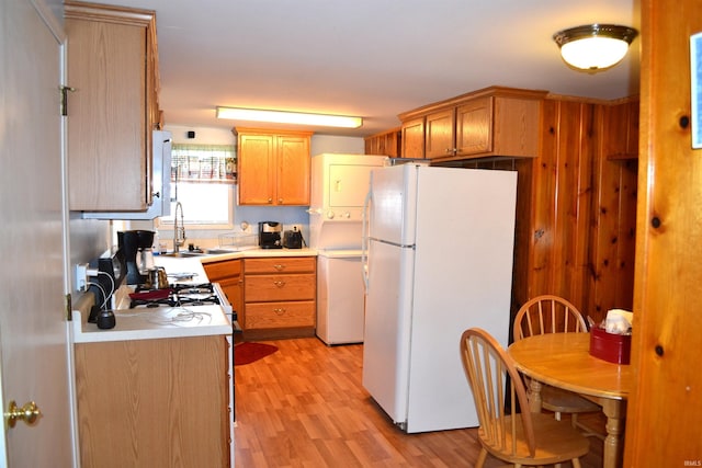 kitchen with light wood finished floors, stacked washing maching and dryer, freestanding refrigerator, a sink, and light countertops