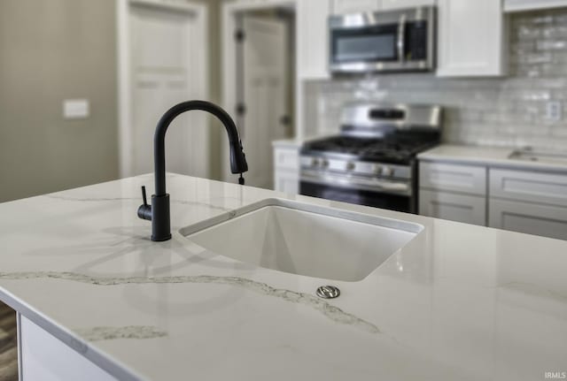 kitchen featuring a sink, tasteful backsplash, white cabinetry, stainless steel appliances, and light stone countertops