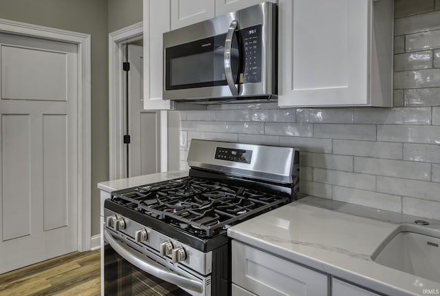 kitchen featuring light wood-type flooring, stainless steel appliances, backsplash, and white cabinetry