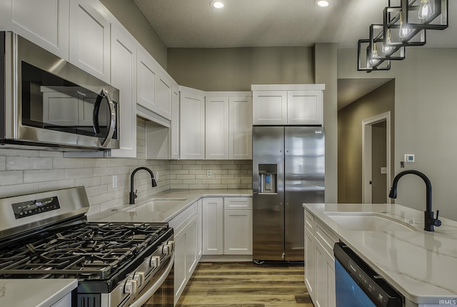 kitchen with a sink, stainless steel appliances, wood finished floors, and white cabinetry