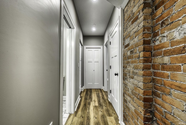 hall featuring brick wall, baseboards, and dark wood-style flooring