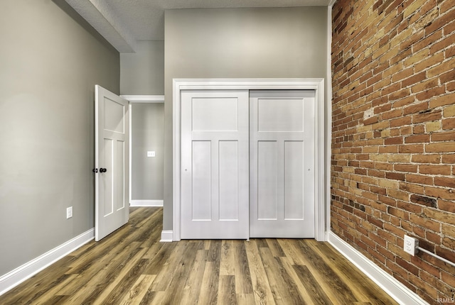 unfurnished bedroom with a closet, baseboards, brick wall, and dark wood-style flooring