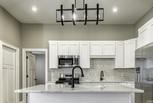 kitchen with backsplash, white cabinetry, stainless steel appliances, and a kitchen island with sink