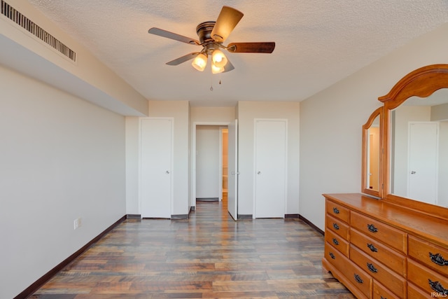 unfurnished bedroom featuring visible vents, a textured ceiling, baseboards, ceiling fan, and dark wood-style flooring