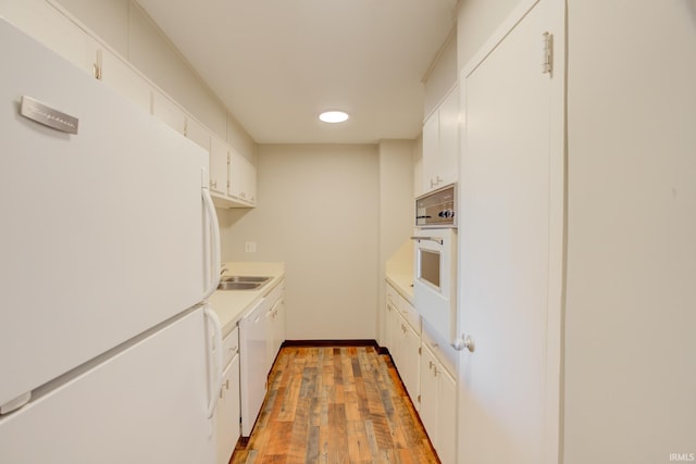 kitchen with light countertops, light wood-style floors, white appliances, white cabinetry, and a sink