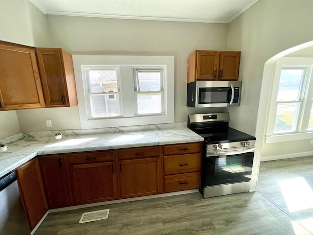 kitchen featuring brown cabinetry, visible vents, arched walkways, ornamental molding, and stainless steel appliances