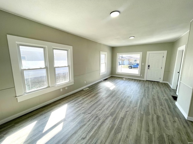 unfurnished living room featuring visible vents, baseboards, a textured ceiling, and wood finished floors