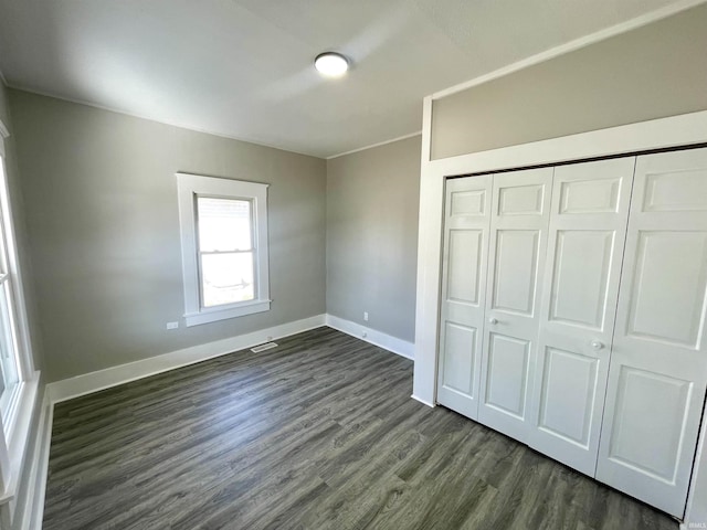 unfurnished bedroom featuring a closet, visible vents, dark wood-type flooring, and baseboards