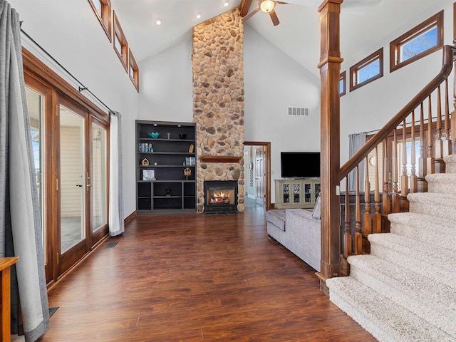 living room featuring visible vents, beamed ceiling, wood finished floors, stairway, and a stone fireplace