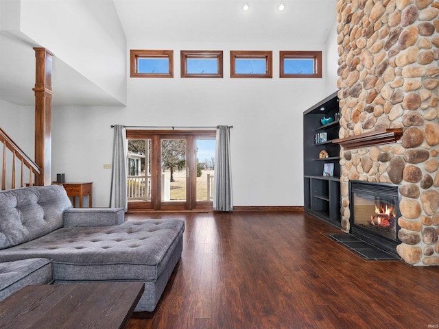 living area with a stone fireplace, stairs, wood finished floors, and high vaulted ceiling