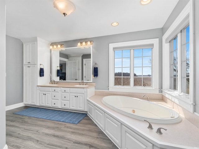 bathroom featuring double vanity, a jetted tub, wood finished floors, and a sink