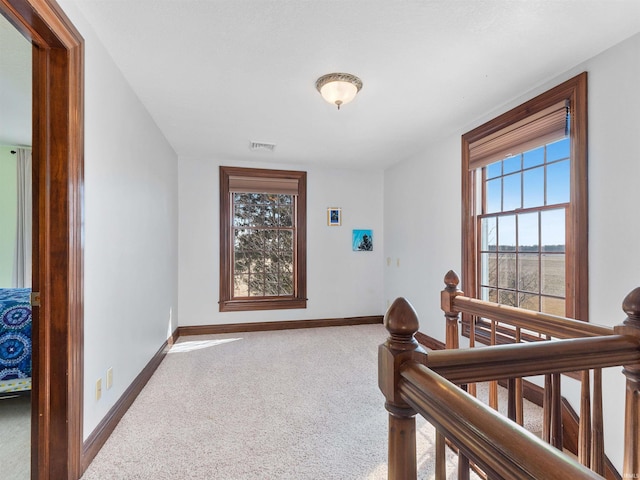 hallway with an upstairs landing, carpet flooring, a healthy amount of sunlight, and visible vents