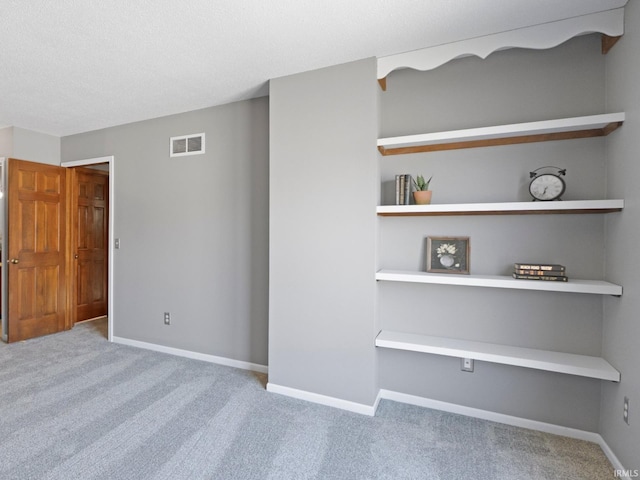 carpeted spare room featuring visible vents, a textured ceiling, and baseboards