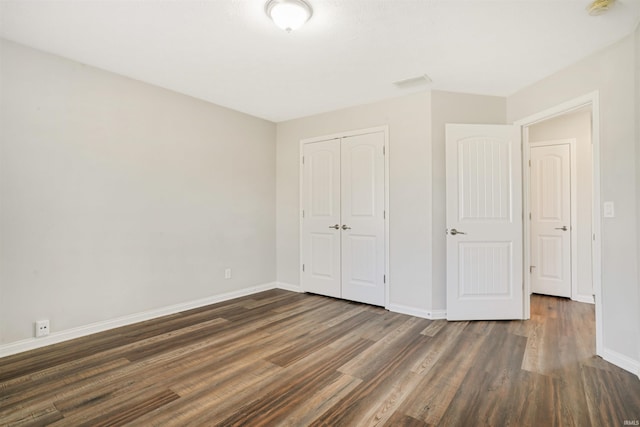 unfurnished bedroom with dark wood finished floors, baseboards, and a closet