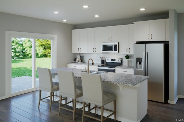 kitchen featuring dark wood finished floors, a kitchen island with sink, a sink, appliances with stainless steel finishes, and backsplash