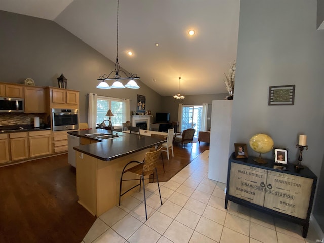 kitchen with dark countertops, light brown cabinets, open floor plan, appliances with stainless steel finishes, and a sink