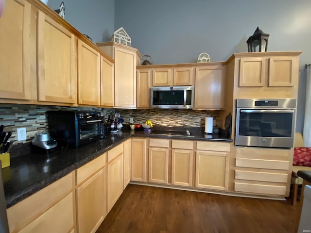 kitchen with light brown cabinets, dark wood-type flooring, dark stone counters, decorative backsplash, and stainless steel appliances