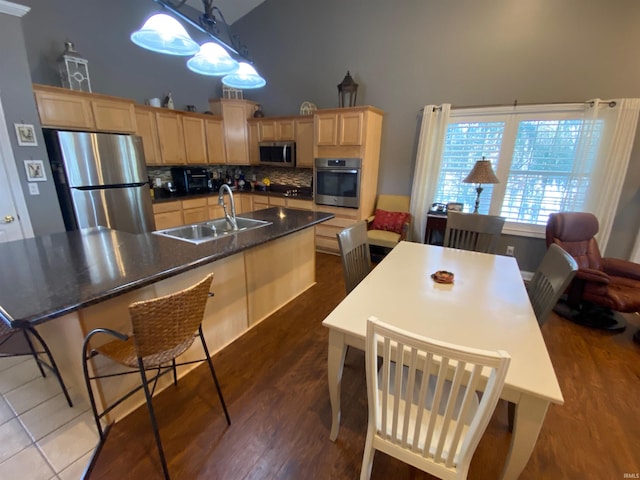 kitchen with dark countertops, a spacious island, light brown cabinets, stainless steel appliances, and a sink