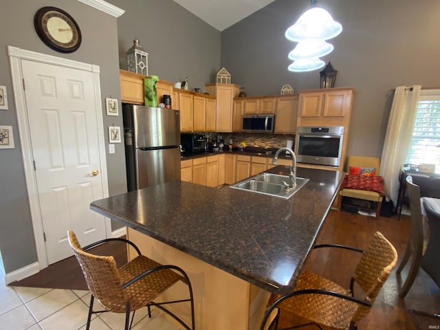 kitchen with high vaulted ceiling, light brown cabinetry, a sink, appliances with stainless steel finishes, and a breakfast bar area