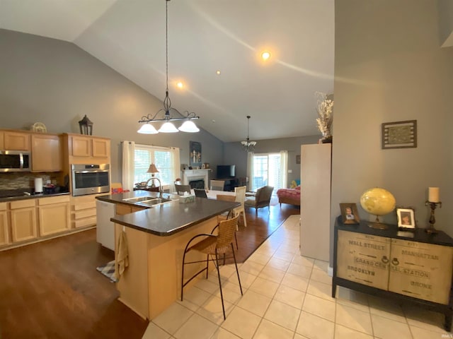 kitchen with light brown cabinets, a sink, appliances with stainless steel finishes, dark countertops, and open floor plan